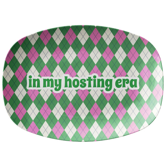 Green and pink argyle pattern printed on a serving platter with text that says in my hosting era.