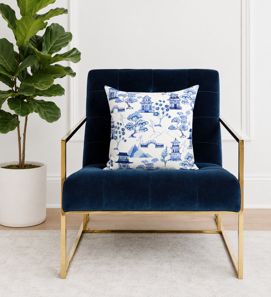 Navy blue armchair with a decorative pillow featuring a blue and white toile pattern, next to a potted plant.