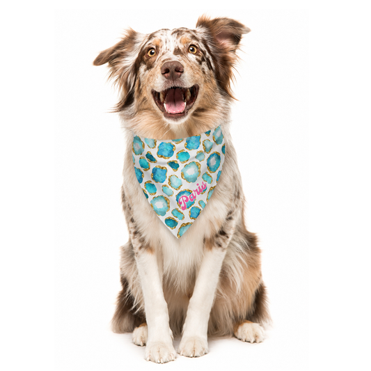 Dog wearing a blue, gold and white jewel patterned bandana with customized name on a white background