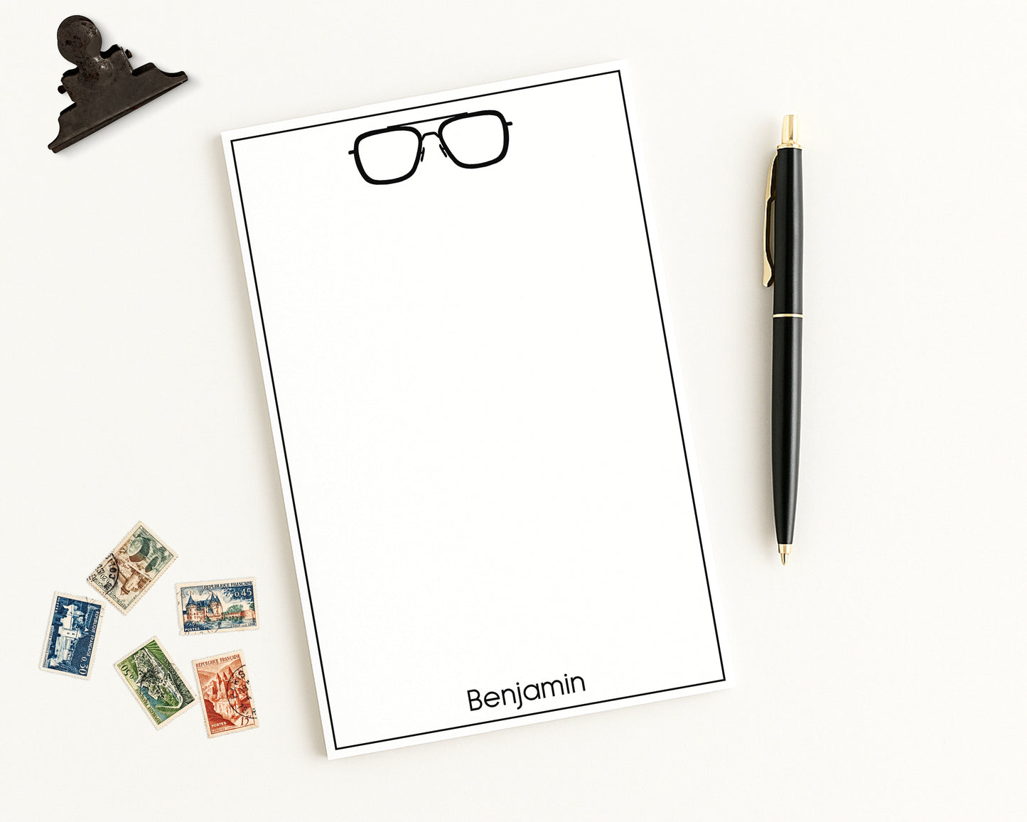 Custom Notepad Stationery with eyeglasses icon and personalized monogram on a white background with a pen and stamps.