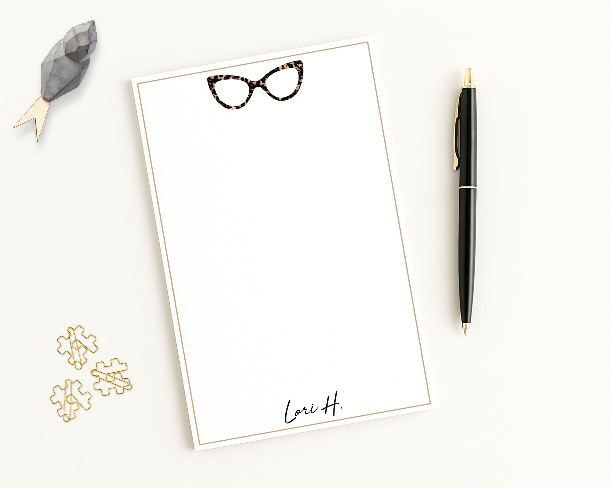 Personalized notepad features cat eye eyeglasses with custom monogram name, and beige border - shown with desk accessories.