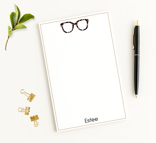 Personalized notepad desk stationery with tortoiseshell eyeglasses design and custom name shown with office accessories and green leaf.
