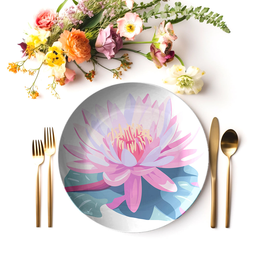Dinner setting with a decorative plate featuring a pink water lily flower design, accompanied by gold cutlery and flowers on a white background.