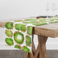 White table runner with green and gold crystal gemstones printed all over it. Shown on a wood table.