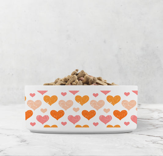 Hearts pattern in orange and pink are printed all around white ceramic pet dish