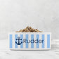 Dog or cat food bowl with blue and white striped pattern and navy blue anchor design with custom name on a marble surface.
