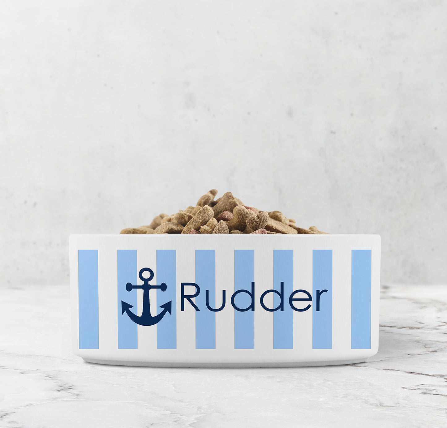 Dog or cat food bowl with blue and white striped pattern and navy blue anchor design with custom name on a marble surface.