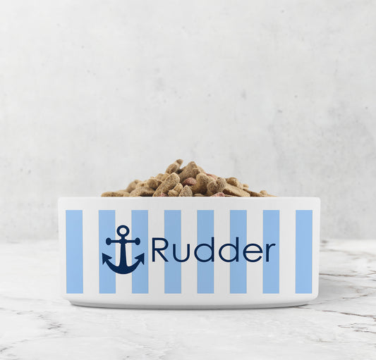 Dog or cat food bowl with blue and white striped pattern and navy blue anchor design with custom name on a marble surface.