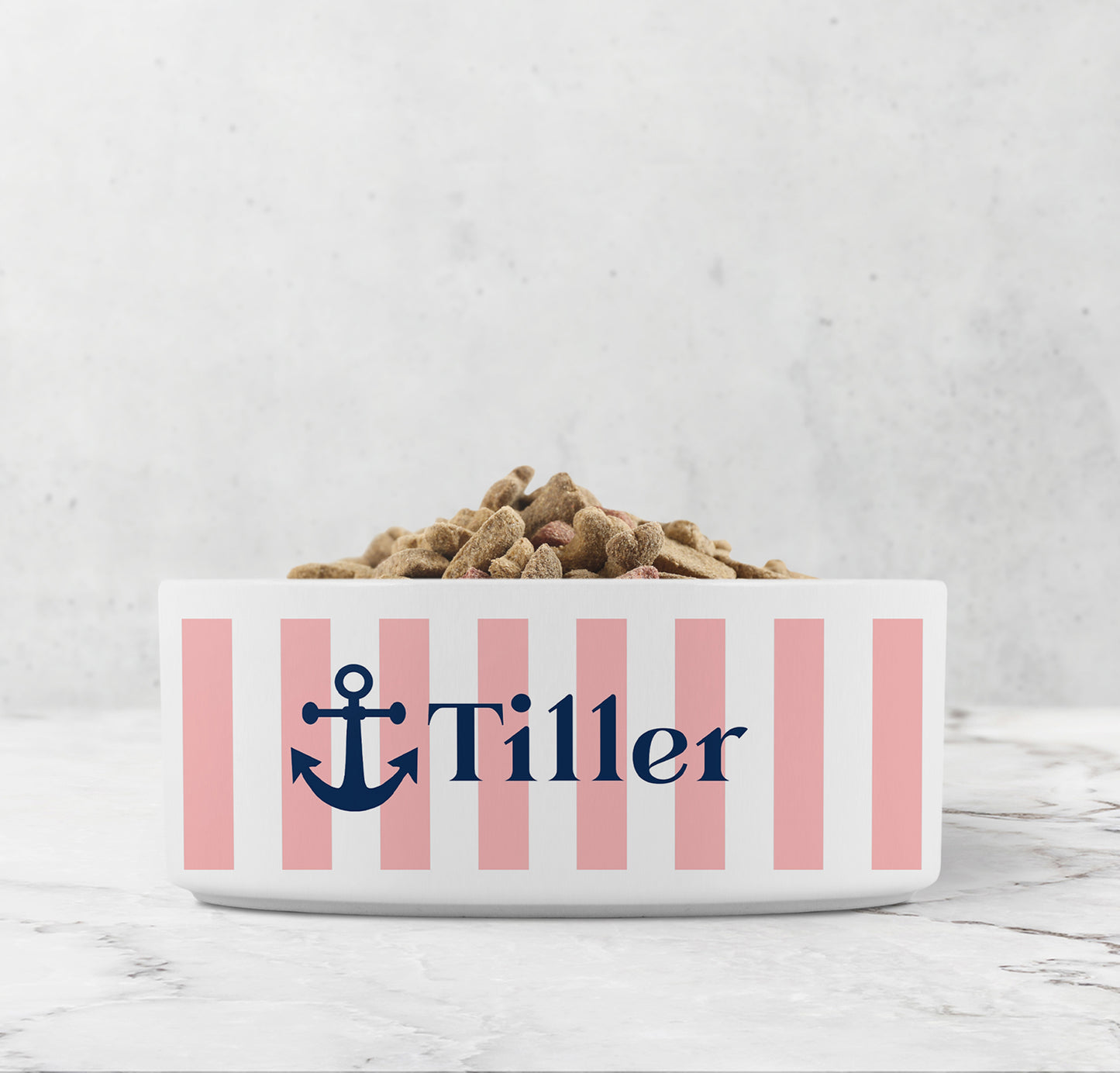 Dog or cat food bowl with pink stripes, Navy Blue anchor and custom pet name on a marble surface.