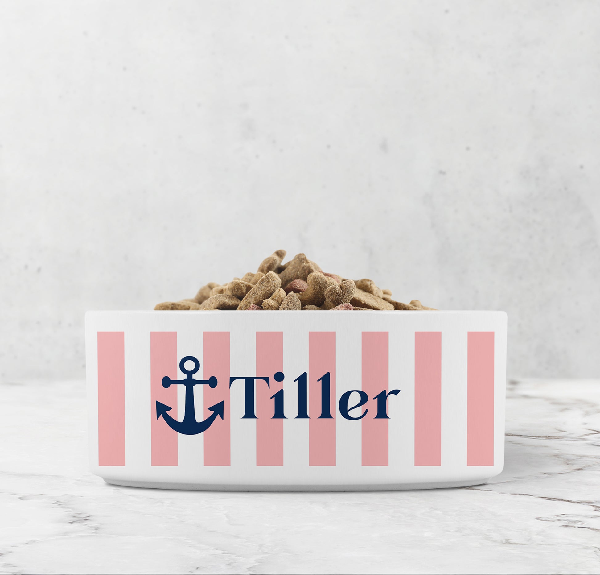 Dog or cat food bowl with pink stripes, Navy Blue anchor and custom pet name on a marble surface.