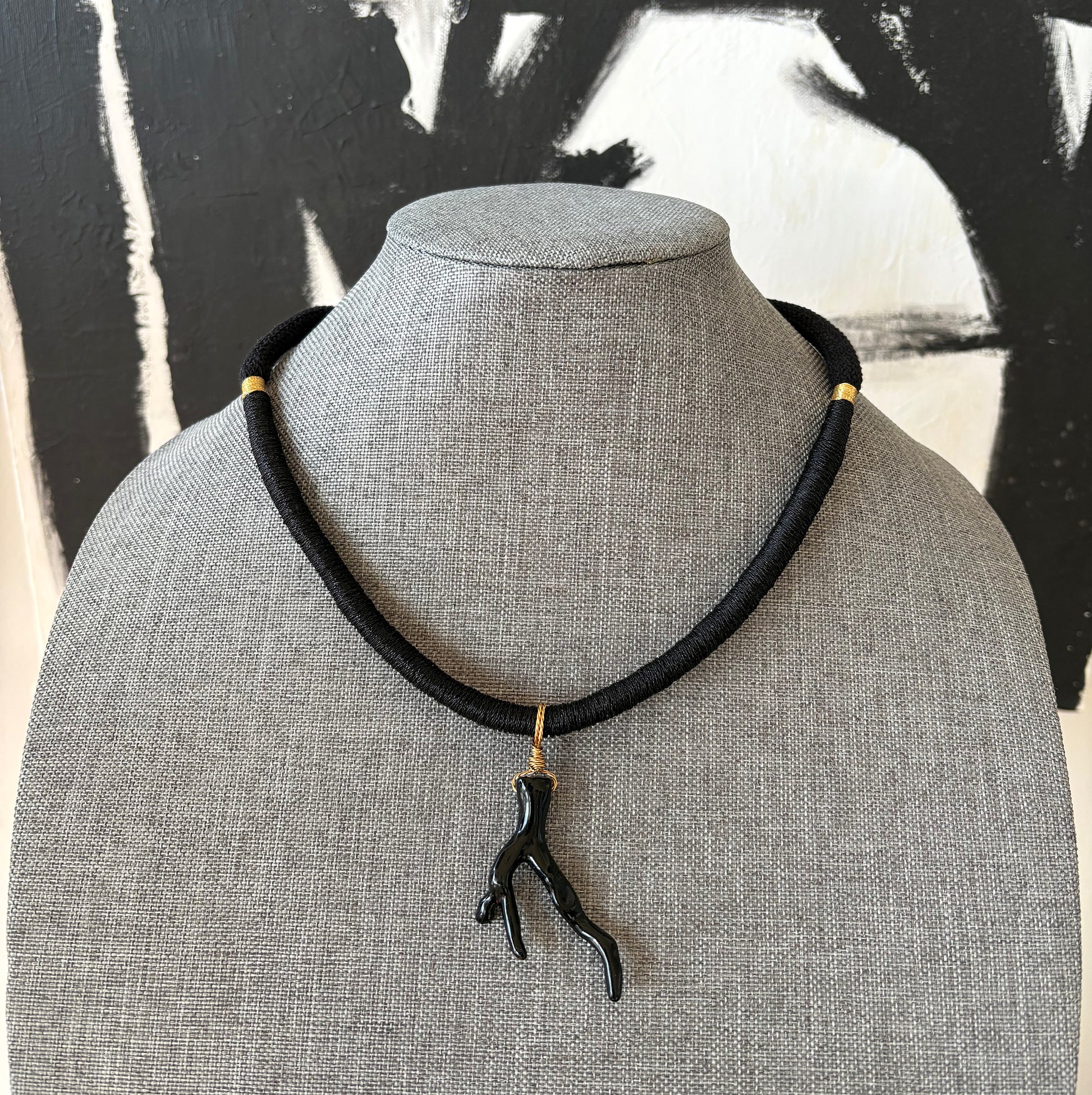 Black rope necklace with a sea coral branch pendant on a gray mannequin against a black and white abstract background