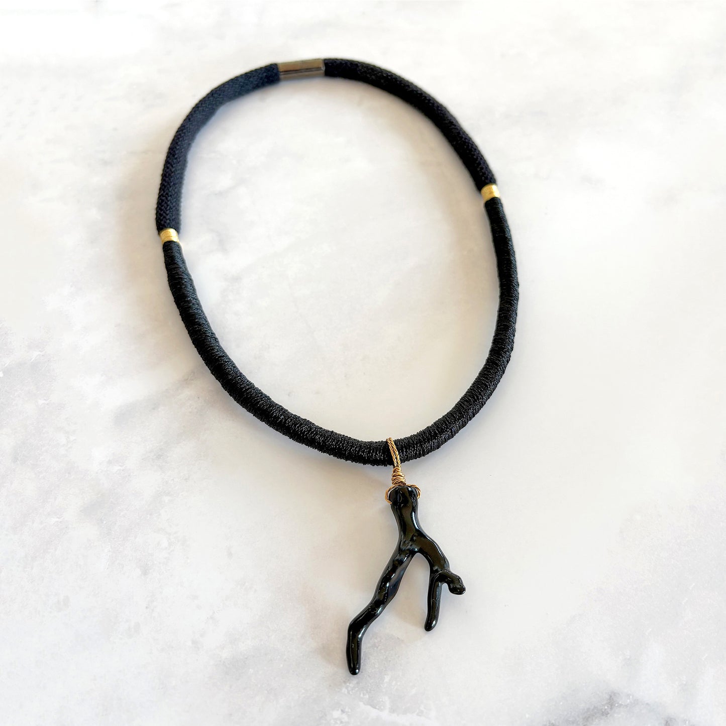 Black braided rope necklace with a sea coral pendant on a white marble surface