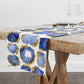 White table runner with blue sapphire and gold crystal gemstones printed all over it. Displayed on a wood table.