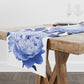 Bold blue peony flower print on white table runner linen draped on a wooden dining table