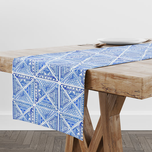 Blue and white hand-drawn geometric tile print table runner on a wooden table.