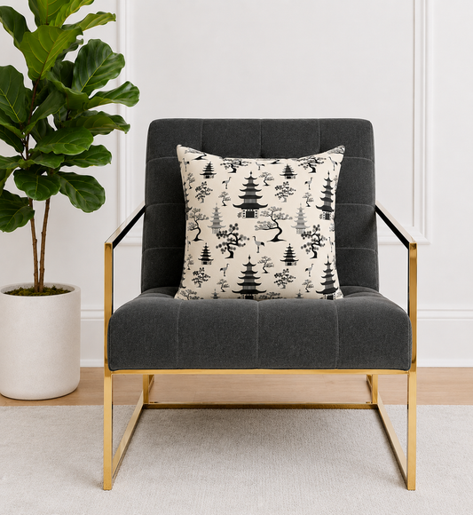 Gray armchair with a decorative warm white pillow featuring black toile pattern, placed in a room with a plant and white walls.