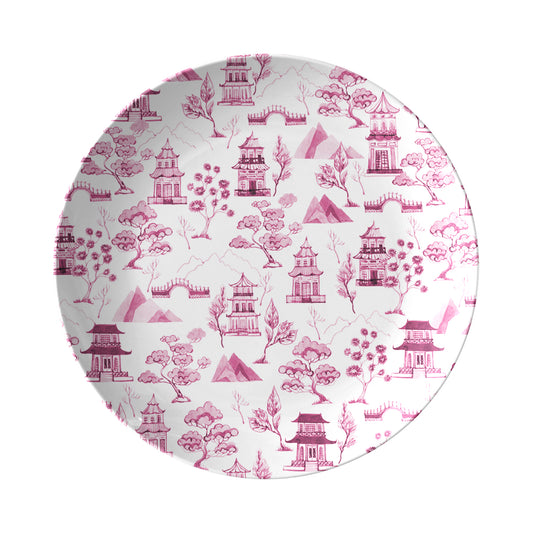 Pink chinoiserie toile plate features pagodas, trees, mountains and bridges printed on a white dinner plate.