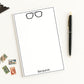 Custom Notepad Stationery with eyeglasses icon and personalized monogram on a white background with a pen and stamps.
