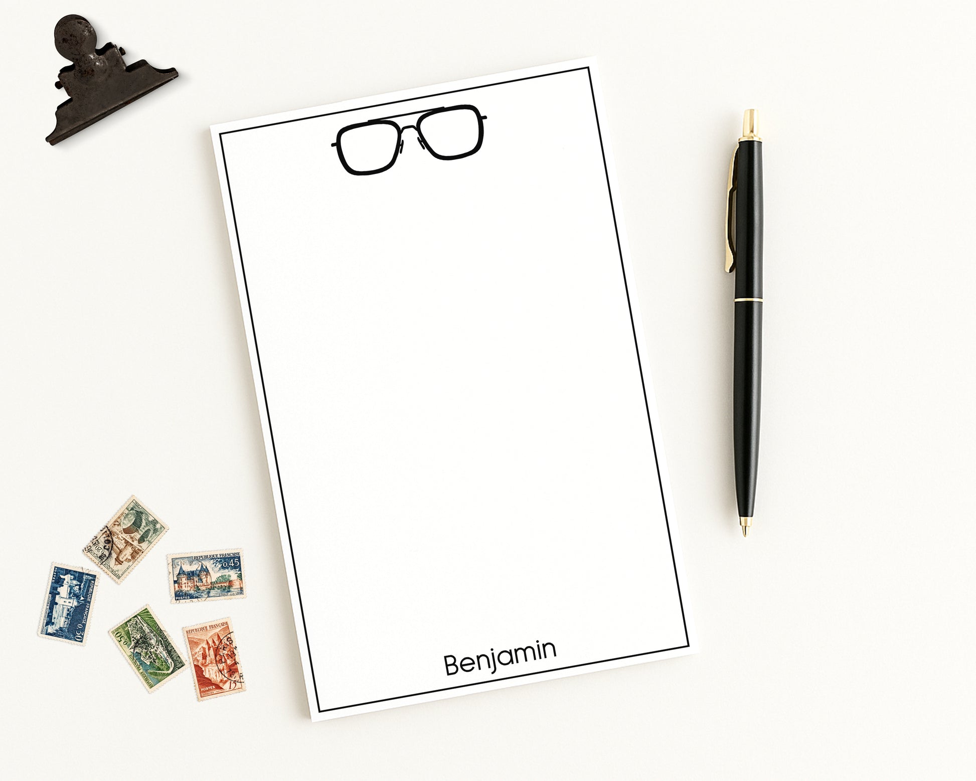 Custom Notepad Stationery with eyeglasses icon and personalized monogram on a white background with a pen and stamps.