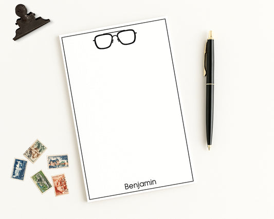 Custom Notepad Stationery with eyeglasses icon and personalized monogram on a white background with a pen and stamps.