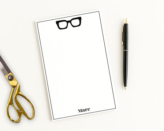 Chunky hipster eyeglasses icon print and custom name on a personalized paper stationery note pad with scissors and pen.
