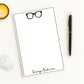 Trendy oversized eyeglasses icon print on personalized notepad with custom name, shown on white desk with candle and accessories.