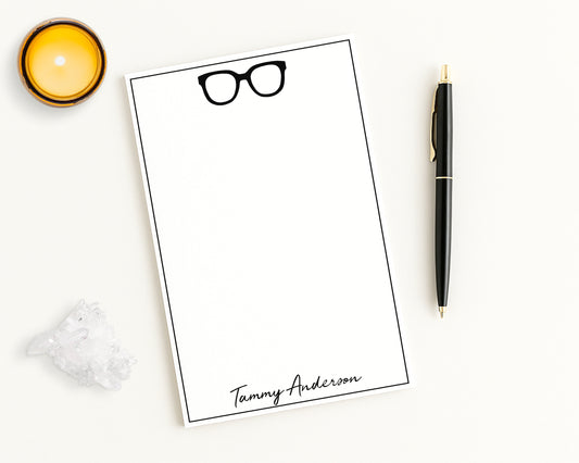 Trendy oversized eyeglasses icon print on personalized notepad with custom name, shown on white desk with candle and accessories.