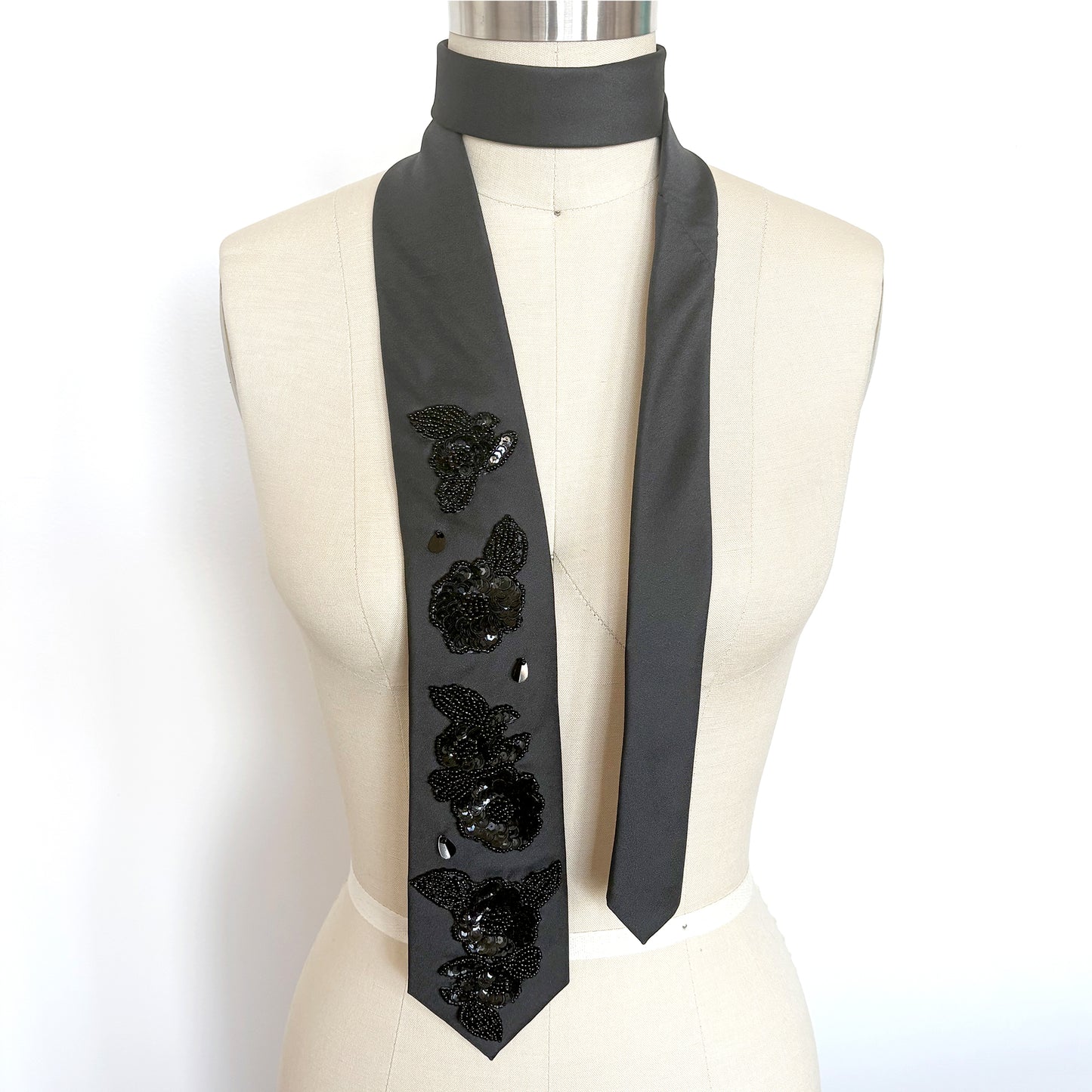 Black embellished necktie scarf with floral beaded sequin appliques draped on a mannequin
