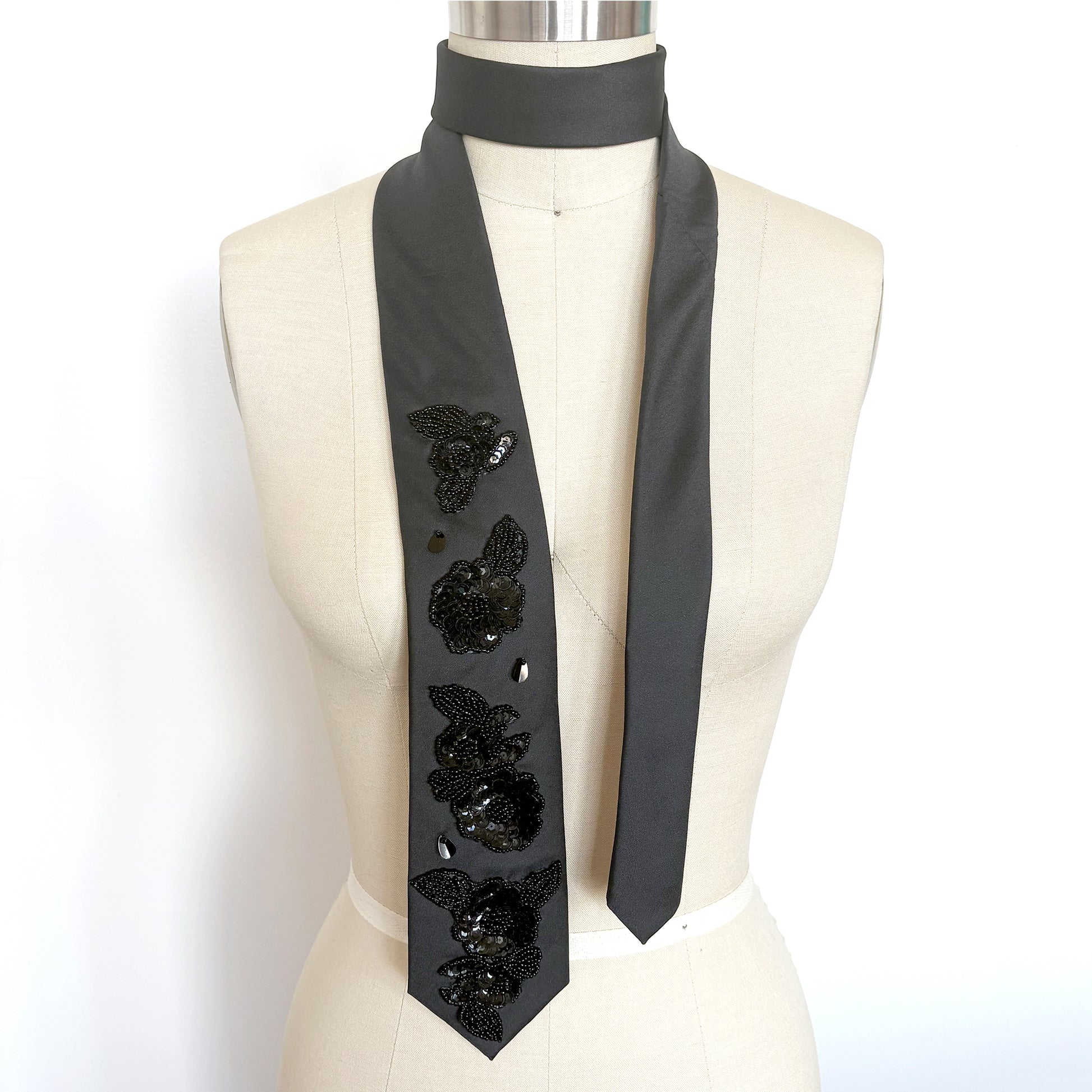 Black embellished necktie scarf with floral beaded sequin appliques draped on a mannequin