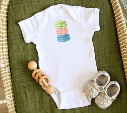 Stacked macaron cookies are printed on a white onesie for babies.