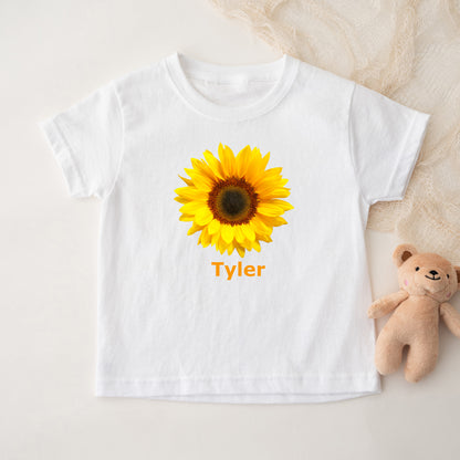 White t-shirt with a sunflower graphic and custom personalized text, accompanied by a teddy bear on a light background