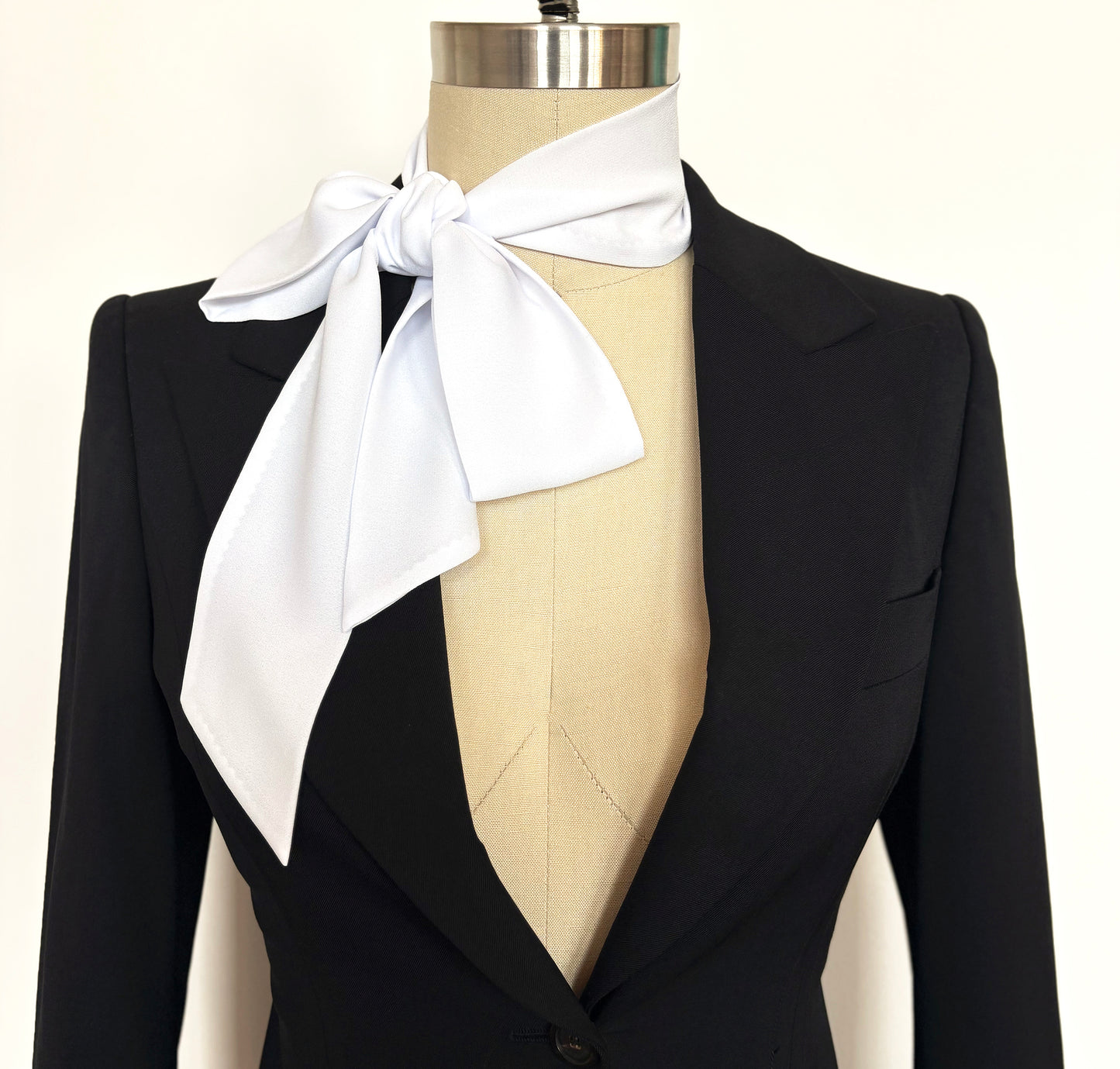 Black blazer with an oversized white bow tie on a mannequin against a white background