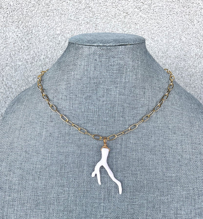 white sea coral pendant on gold paperclip chain on grey jewelry display 