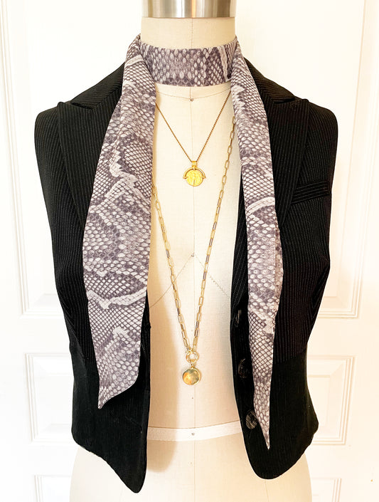 Long skinny twilly scarf with grey snakeskin print worn with vest and layered necklaces.