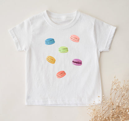 A white toddler t-shirt with a graphic print of colorful macaron cookies.