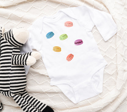 Colorful macaron cookie graphic is printed on a baby onesie in white.